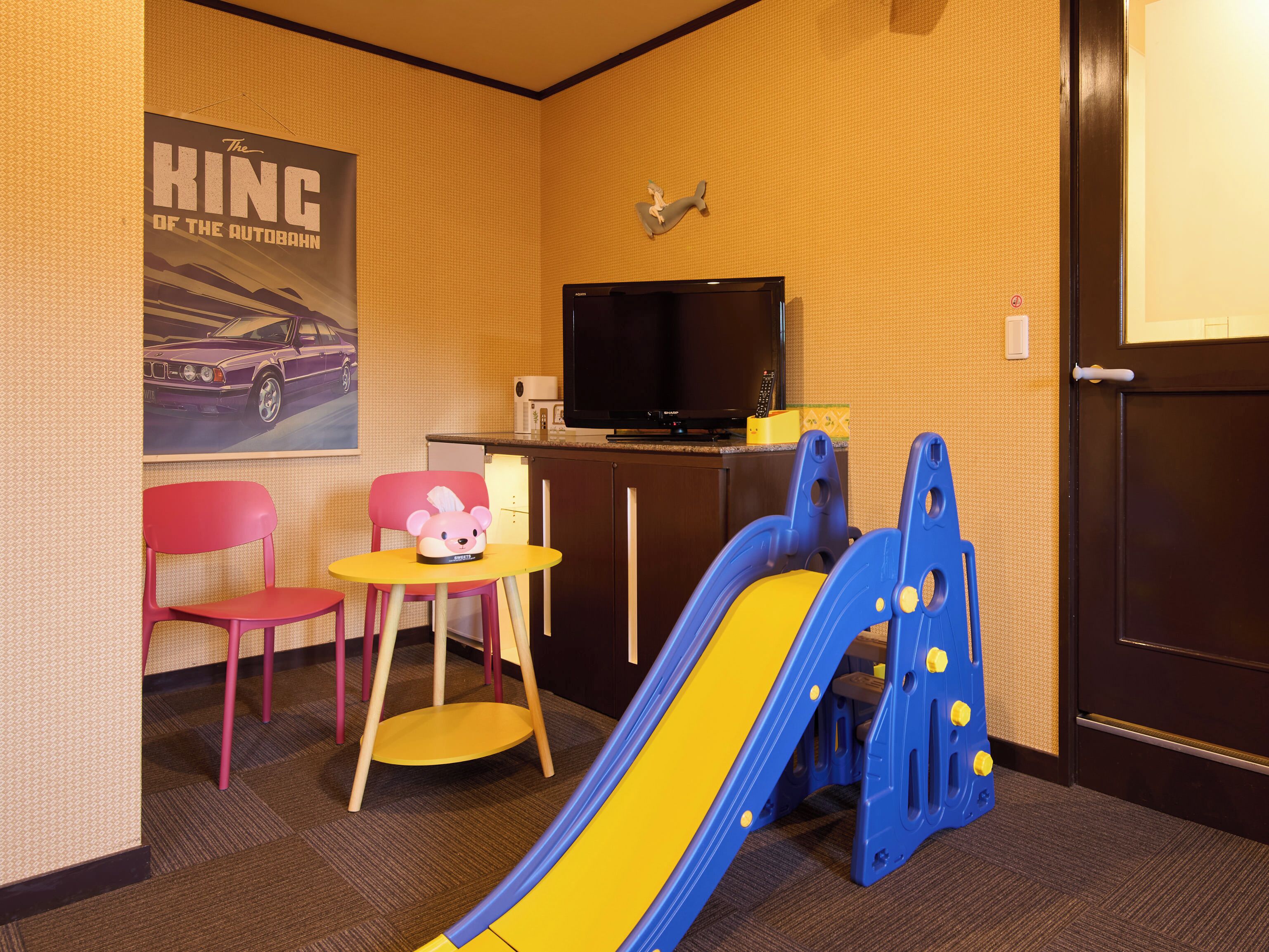 A children's play area with a slide, a small table with a toy, and a TV in the corner.