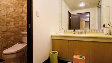 A bathroom with a stone wall, a toilet, a sink with a mirror, and a trash bin.