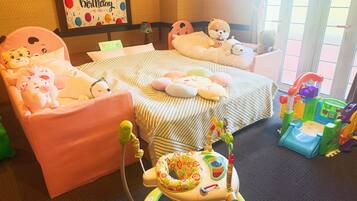 Een kinderkamer met een bed, twee stoelen, een speeltafeltje en een wieg.