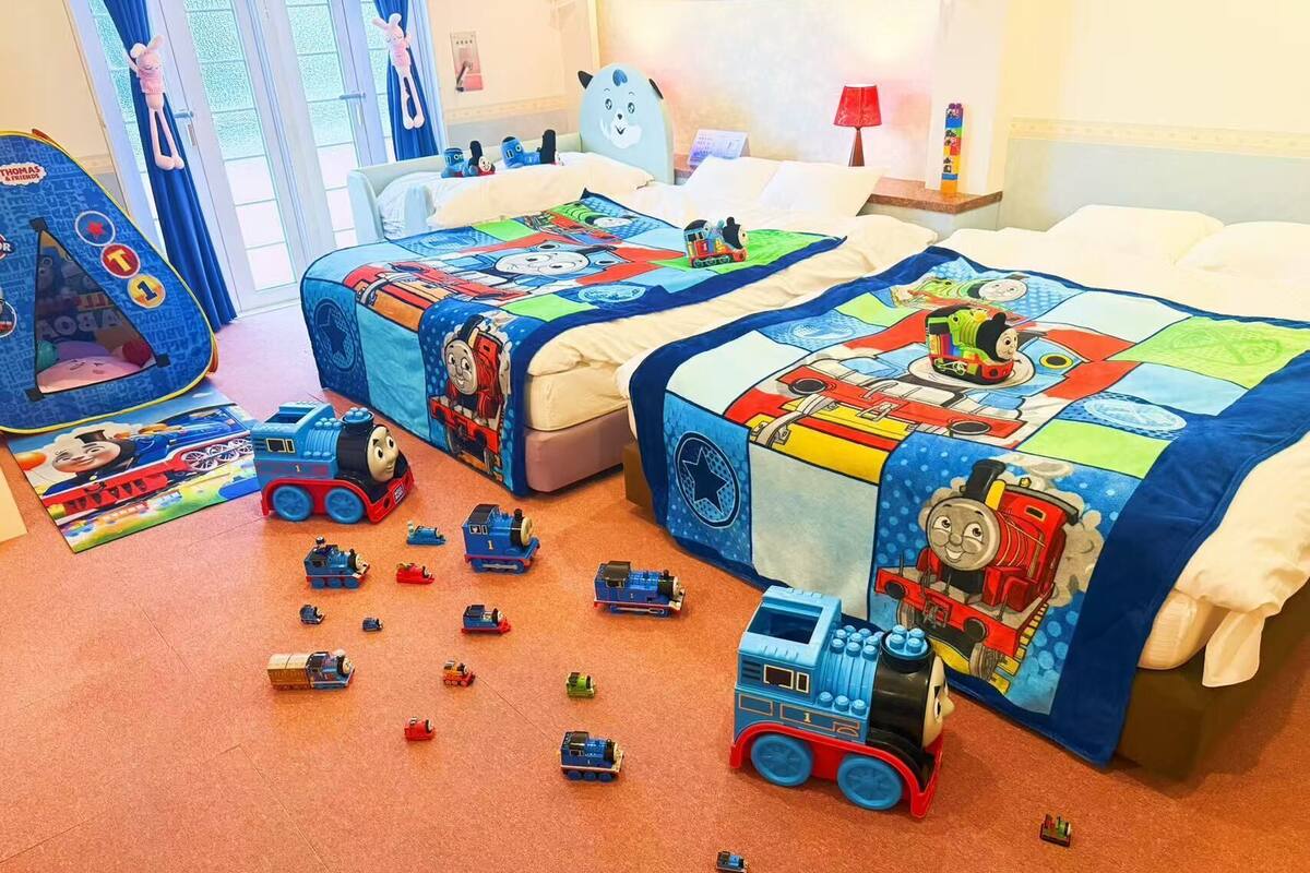 A child's bedroom with two beds, a play area with Thomas the Tank Engine toys, and a blue play tent.