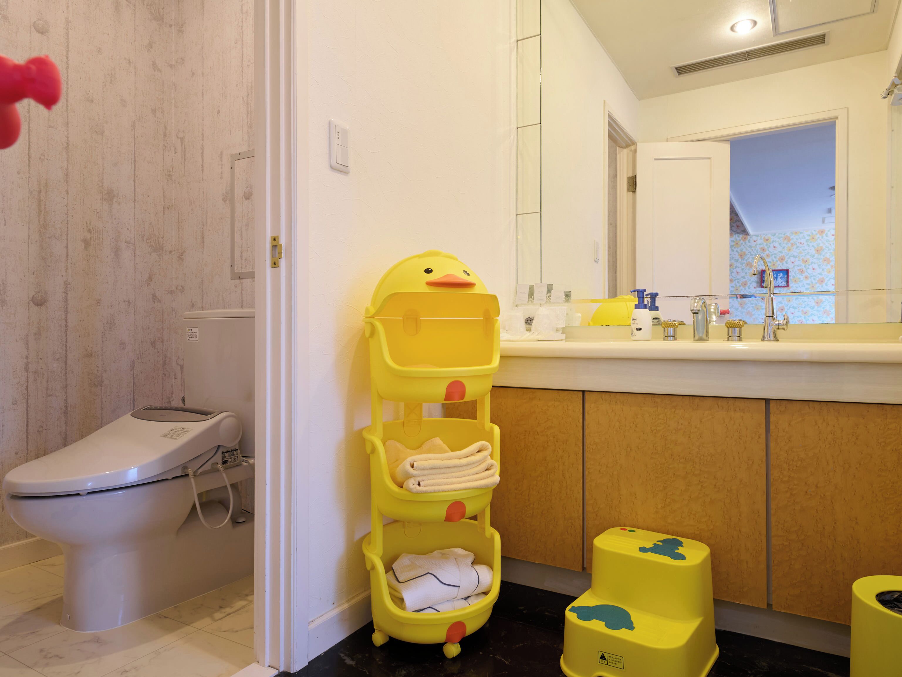 A bathroom with a toilet, a sink with toiletries, and a yellow step stool.