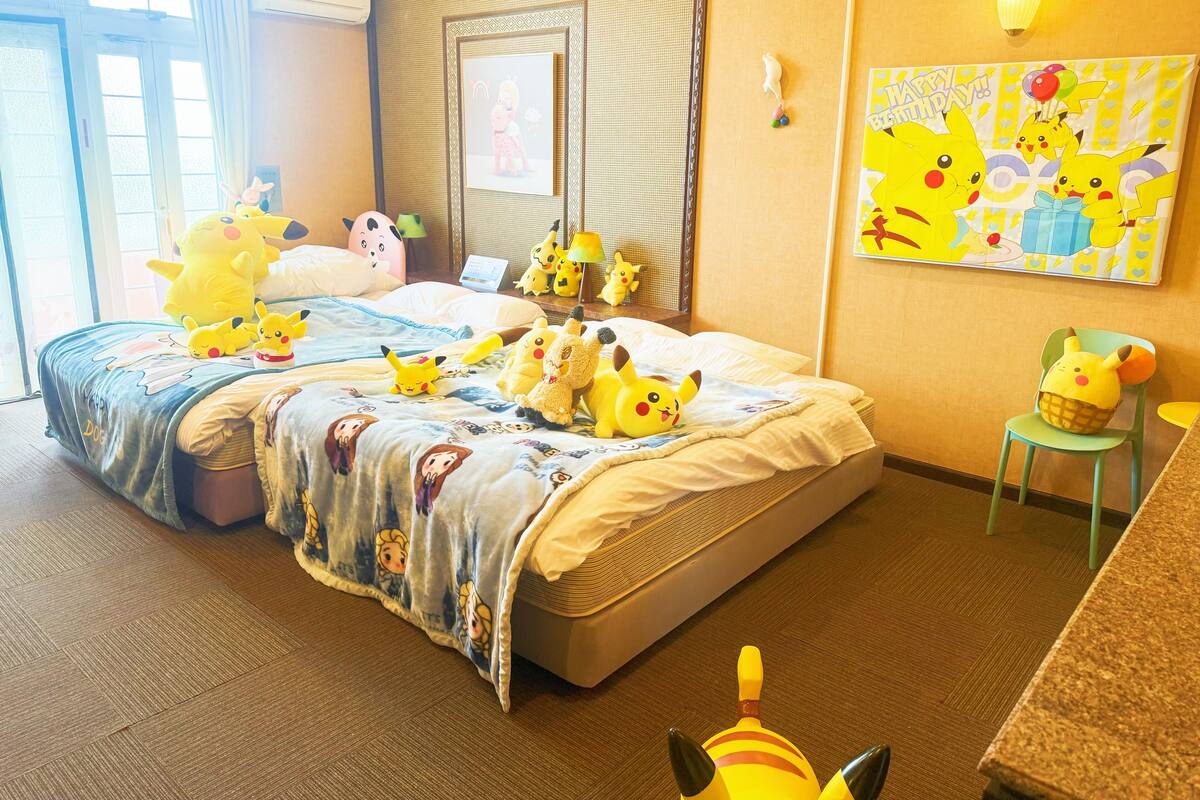 A hotel room with a bed, pillows, and a Pikachu plush toy.