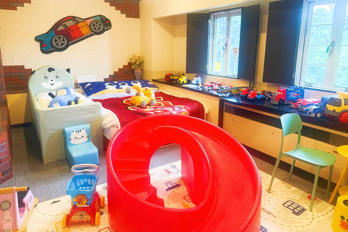 A child's playroom with a bed, a red slide, and a window with toys on the sill.