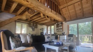A spacious living room with a high wooden ceiling, a sofa set, a coffee table, and a kitchen area visible through an open door. - Romantic Stone Cottage Overlooking Pond. 5mins to Town (Burradoo)
