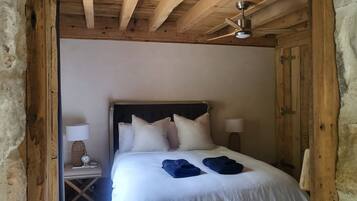 Dormitorio con estructura de madera, cama, almohadas, mesita de noche, lámpara y ventilador de techo.