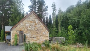 A stone cottage with a sloped roof, surrounded by a garden with various plants and flowers. - Romantic Stone Cottage Overlooking Pond. 5mins to Town (Burradoo)