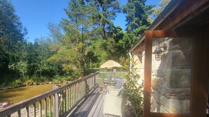 A wooden deck with a stone wall and a thatched umbrella. - Romantic Stone Cottage Overlooking Pond. 5mins to Town (Burradoo)
