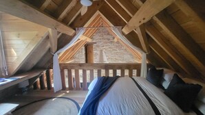 A cozy attic bedroom with a sloped ceiling, wooden beams, a stone wall, and a bed with pillows. - Romantic Stone Cottage Overlooking Pond. 5mins to Town (Burradoo)
