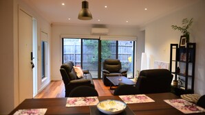 A living room with a sofa, chairs, a dining table with placemats, and a bookshelf.