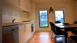 A modern kitchen with white cabinets, a dishwasher, and an oven. There is a dining area with a table and chairs, and a window providing a view of the outside.