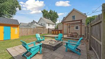 Patio trasero con un brasero, cuatro sillas y una pérgola de madera.