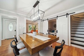 A dining area with a wooden table, chairs, a hanging light fixture, and a sliding barn door.