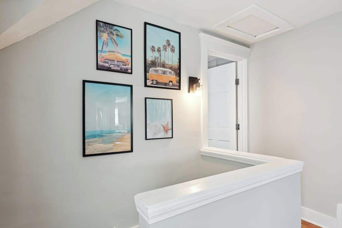 Un pasillo con una pared blanca, un banco blanco y cuatro cuadros enmarcados que muestran escenas de playa.