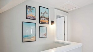 Un pasillo con una pared blanca, un banco blanco y cuatro cuadros enmarcados que muestran escenas de playa.
