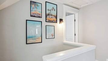 Un pasillo con una pared blanca, un banco blanco y cuatro cuadros enmarcados que muestran escenas de playa.