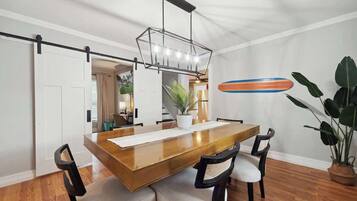 Un comedor con una mesa de madera, cuatro sillas, una lámpara colgante y una planta en maceta.