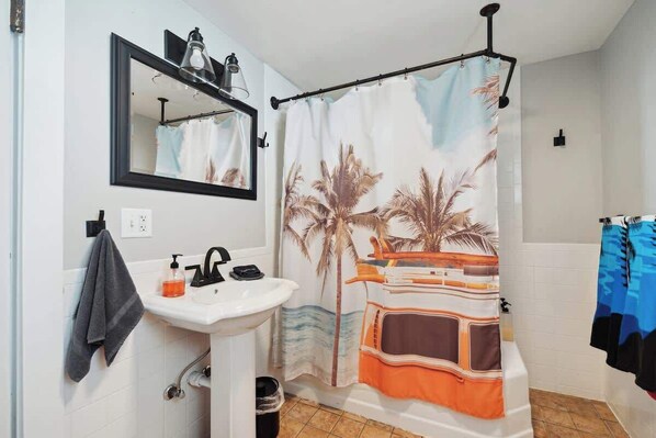 A bathroom with a white sink, a mirror, a towel rack, and a shower curtain with a palm tree design.