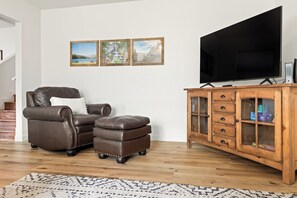 Una sala de estar con un sofá de cuero, un reposapiés, un mueble de madera y un televisor de pantalla plana grande.