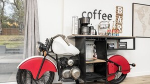 Una motocicleta roja y blanca vintage con una máquina de café y un bar al fondo.