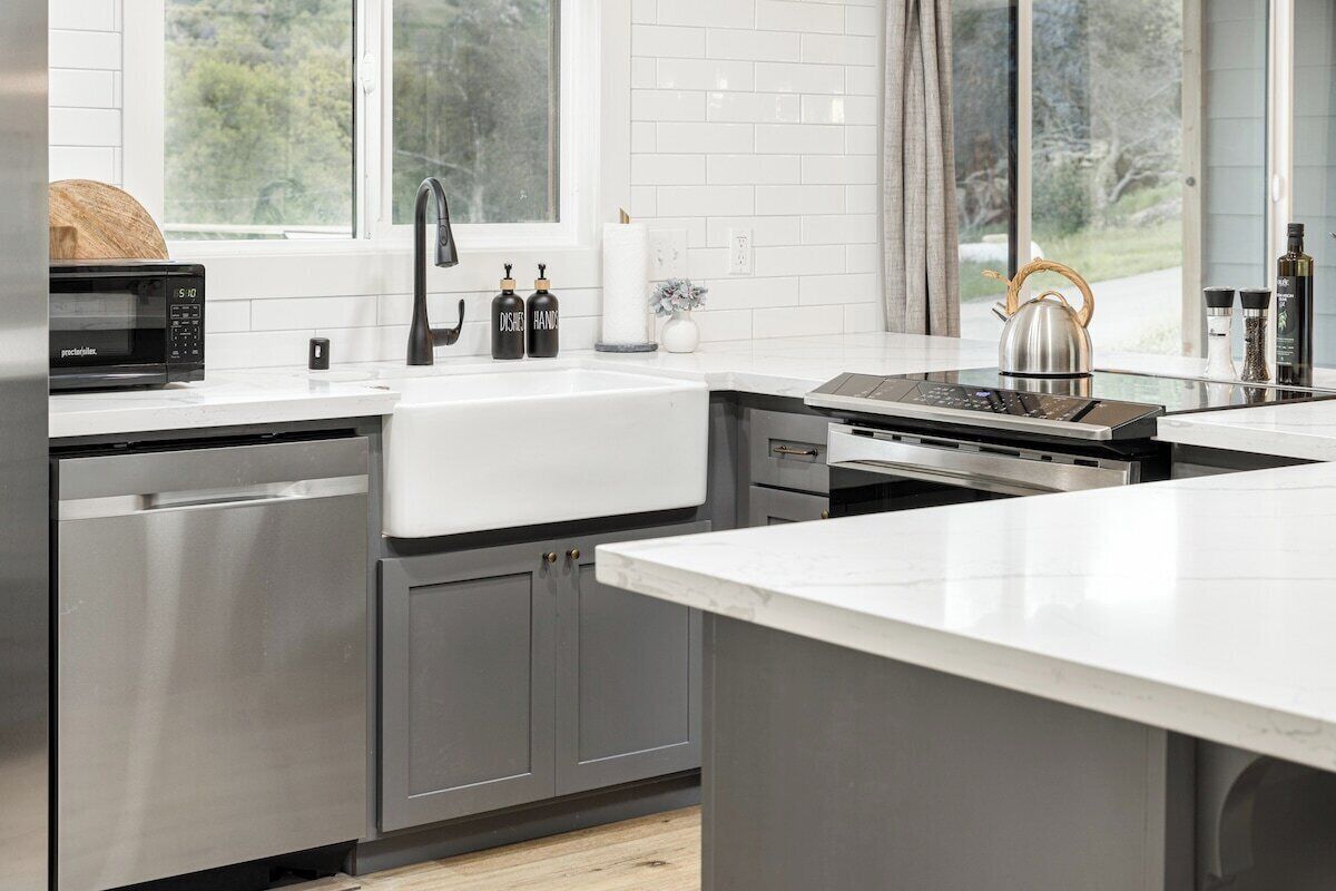 A modern kitchen with stainless steel appliances, a white countertop, and a window providing a view of greenery.