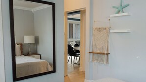 A bedroom with a large mirror, a bed, a nightstand, and a wall-mounted shelf with a starfish decoration.