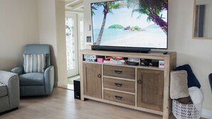 A living room with a television on a wooden cabinet, a grey armchair, and a white woven basket.