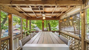 Een houten terras met een tafel en stoelen, grote ramen en een plafondventilator.