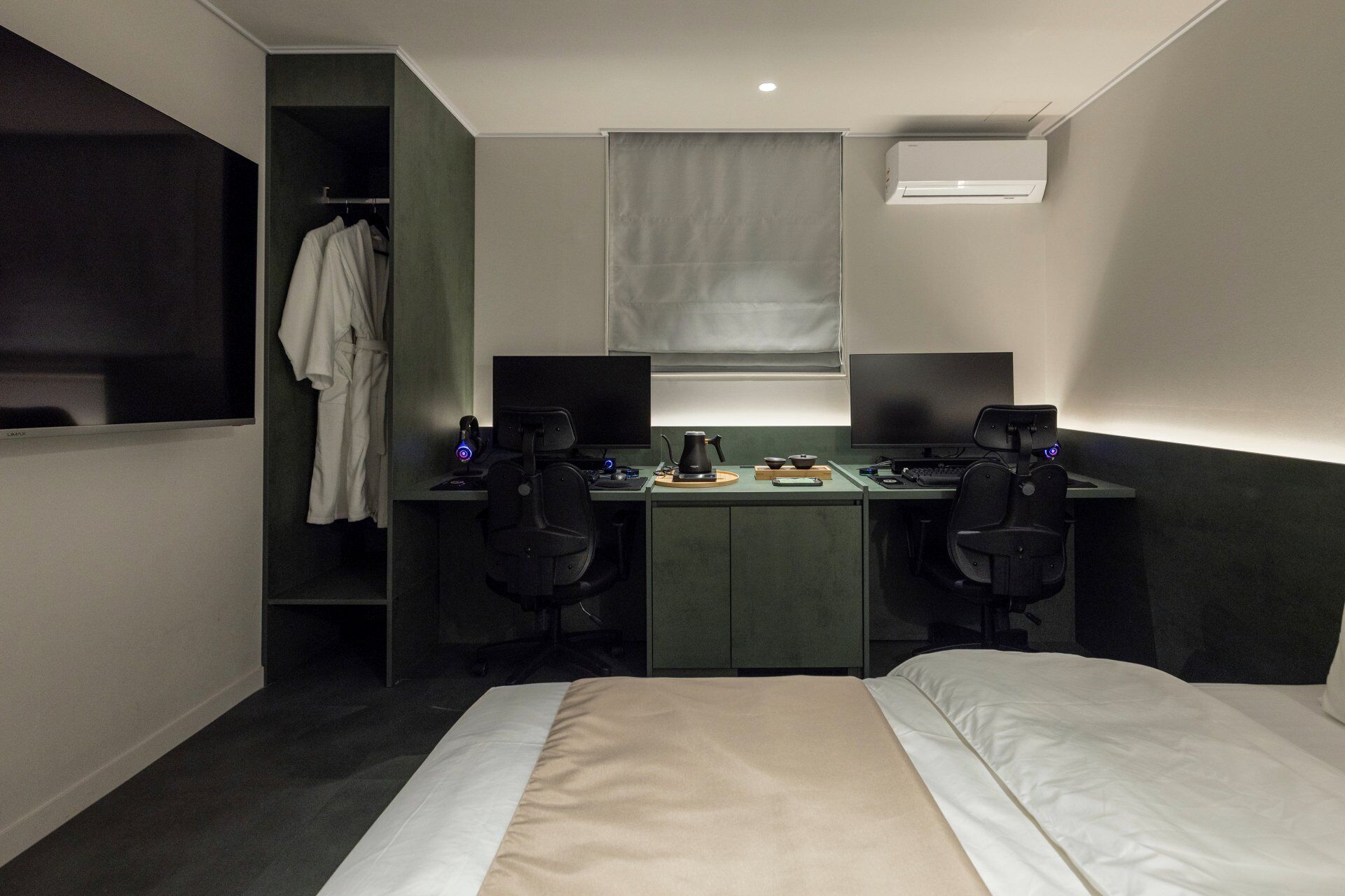 Ein kleines Hotelzimmer mit einem Bett, zwei Schreibtischen mit Computern, einer Kaffeemaschine und einem Kleiderschrank.
