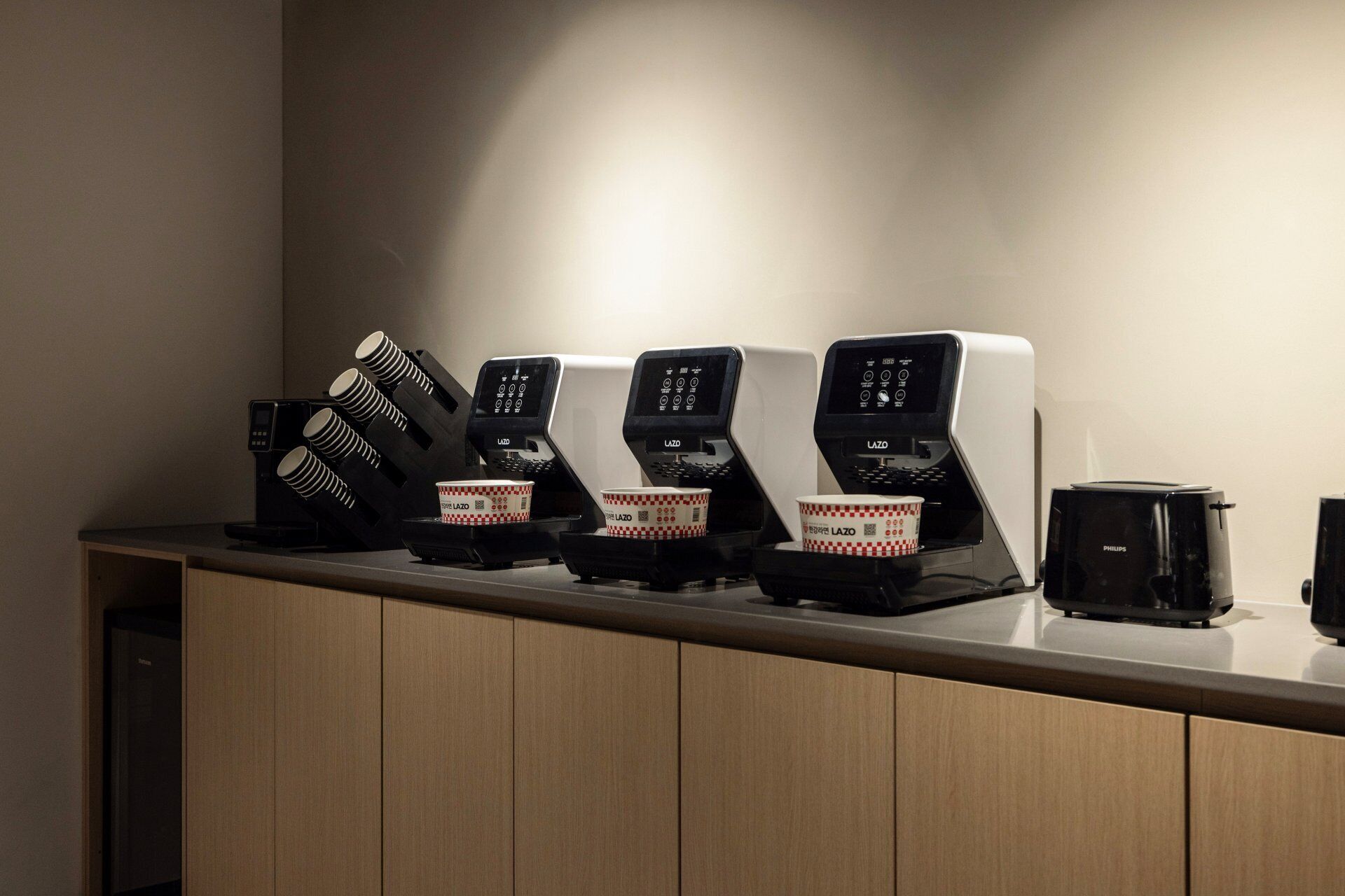 A row of coffee machines with disposable cups on a counter.
