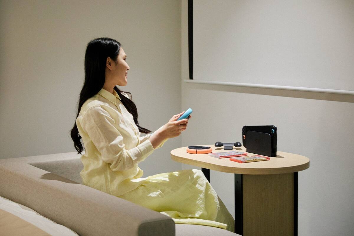 Une personne est assise sur un canapé dans une pièce où se trouvent une petite table ronde, un projecteur fixé au mur et une tablette.