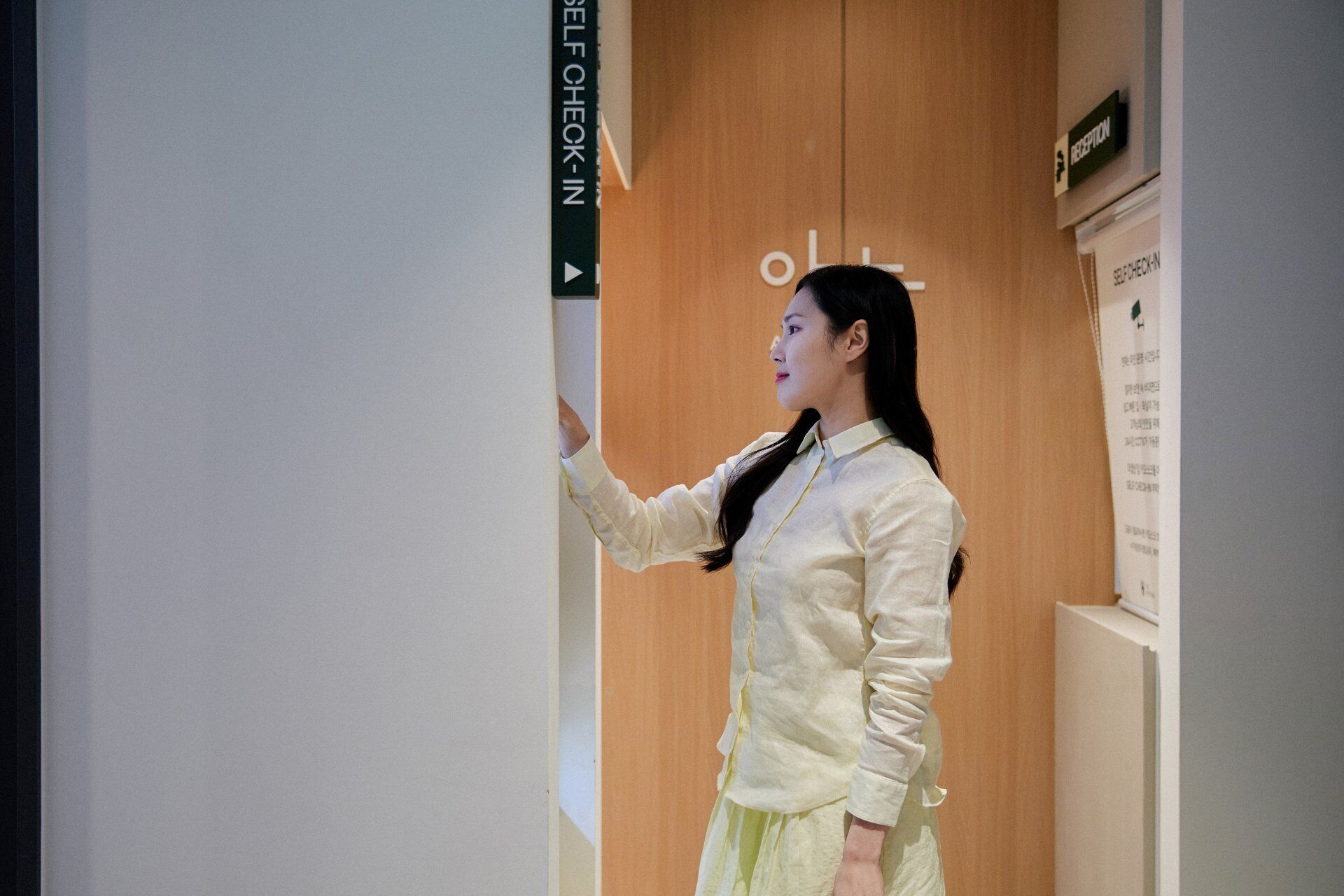 A person standing in a hallway with a sign that reads 'SELF CHECK-IN'.