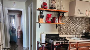 A kitchen with a stove, sink, and shelves with kitchen appliances. - Lil Beachy (Memphis)