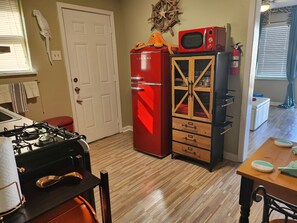 A kitchen with a red refrigerator, a wooden cabinet with drawers, a gas stove, and a dining table with chairs.