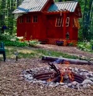 Situated in a forested area, this cabin features a fire pit surrounded by rocks.