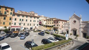 A parking lot with several cars, a church with a bell tower, and a row of buildings with shops and cafes.