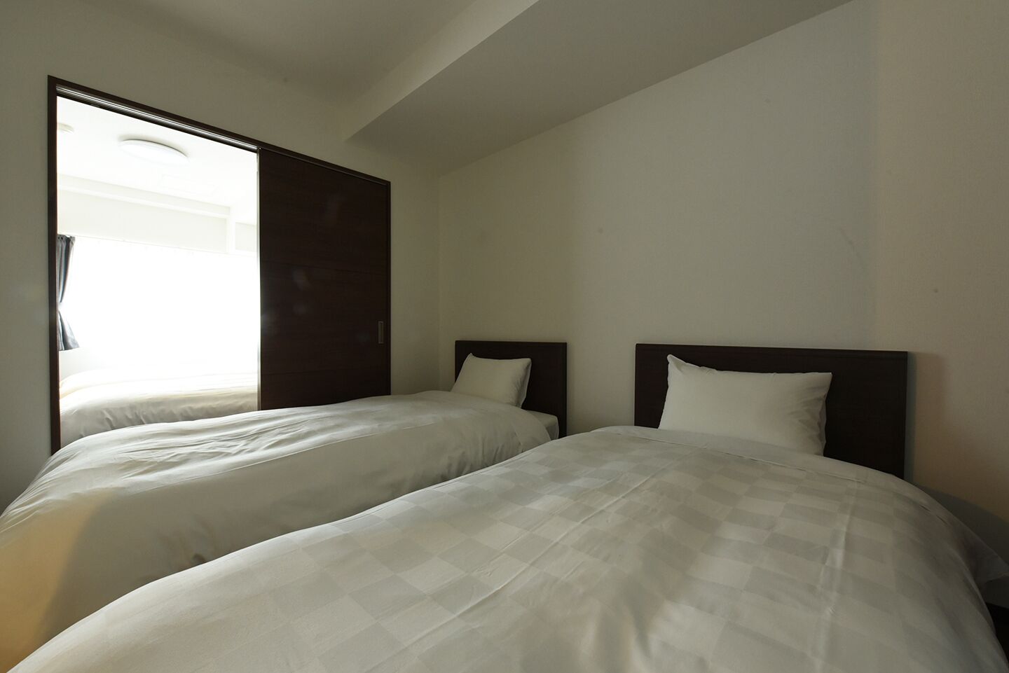 Una habitación de hotel con dos camas individuales, un ventanal grande y una puerta que da a un balcón.