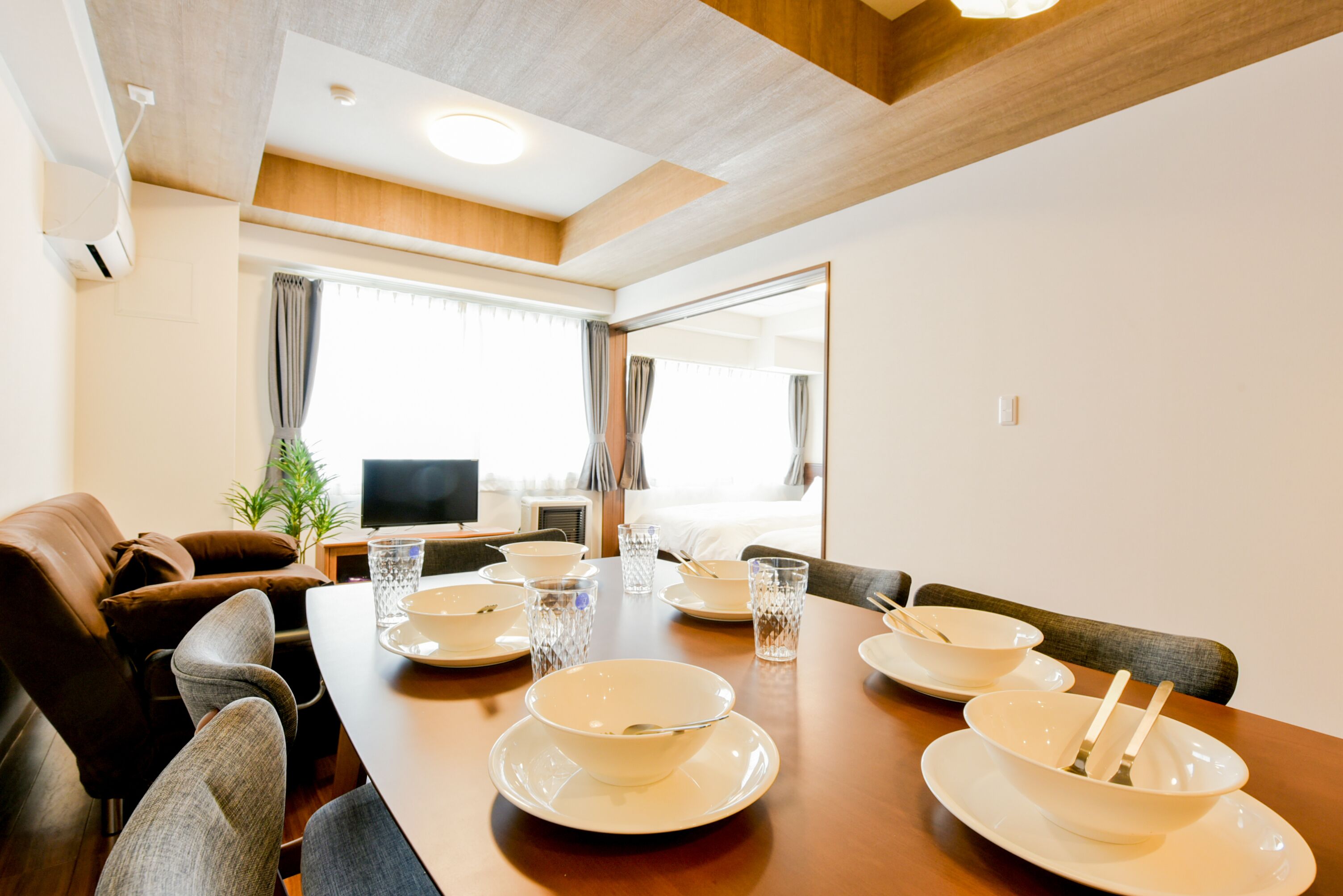 Un coin repas avec une table en bois dressée pour quatre personnes, un canapé et un téléviseur en arrière-plan.