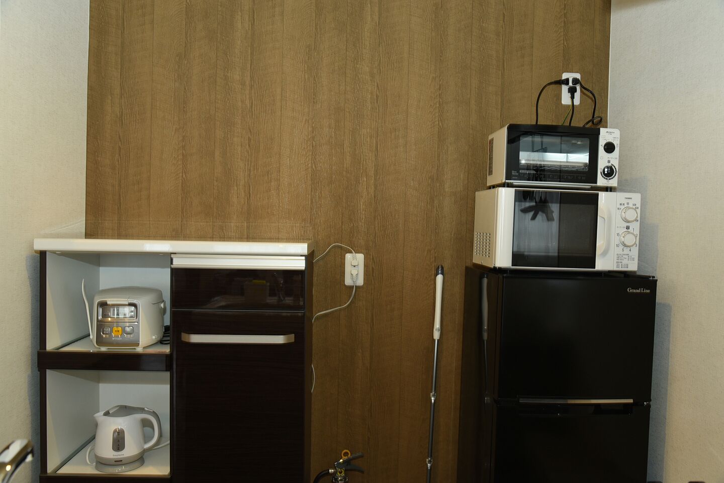 A compact kitchen with a microwave on top of a black refrigerator, a toaster, and a kettle on a shelf.