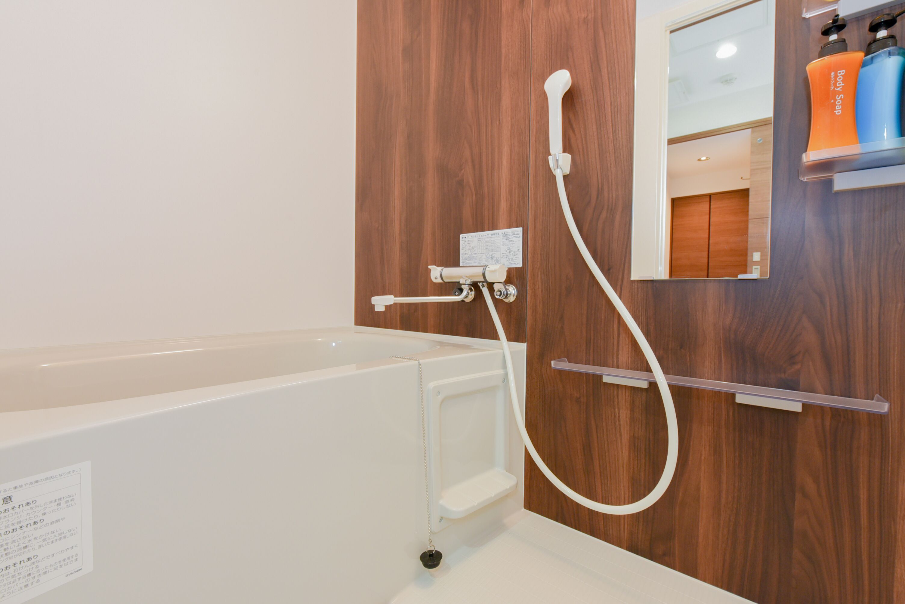 A modern bathroom with a white bathtub, a wooden wall, and a shelf with body soap bottles.