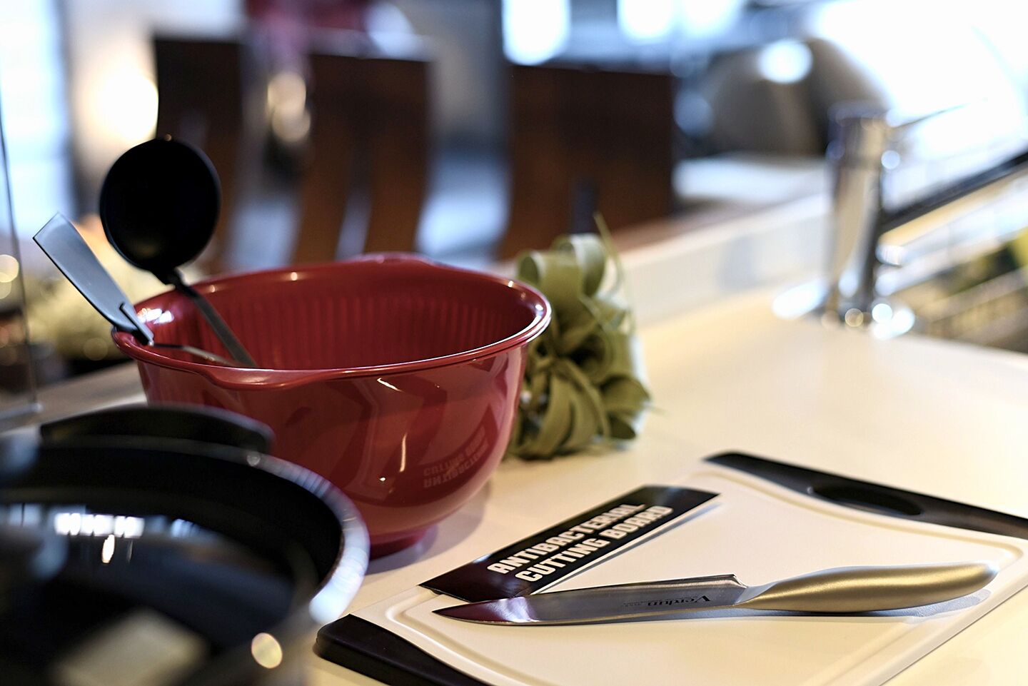 A kitchen counter with a red mixing bowl, a pair of scissors, and a cutting board.