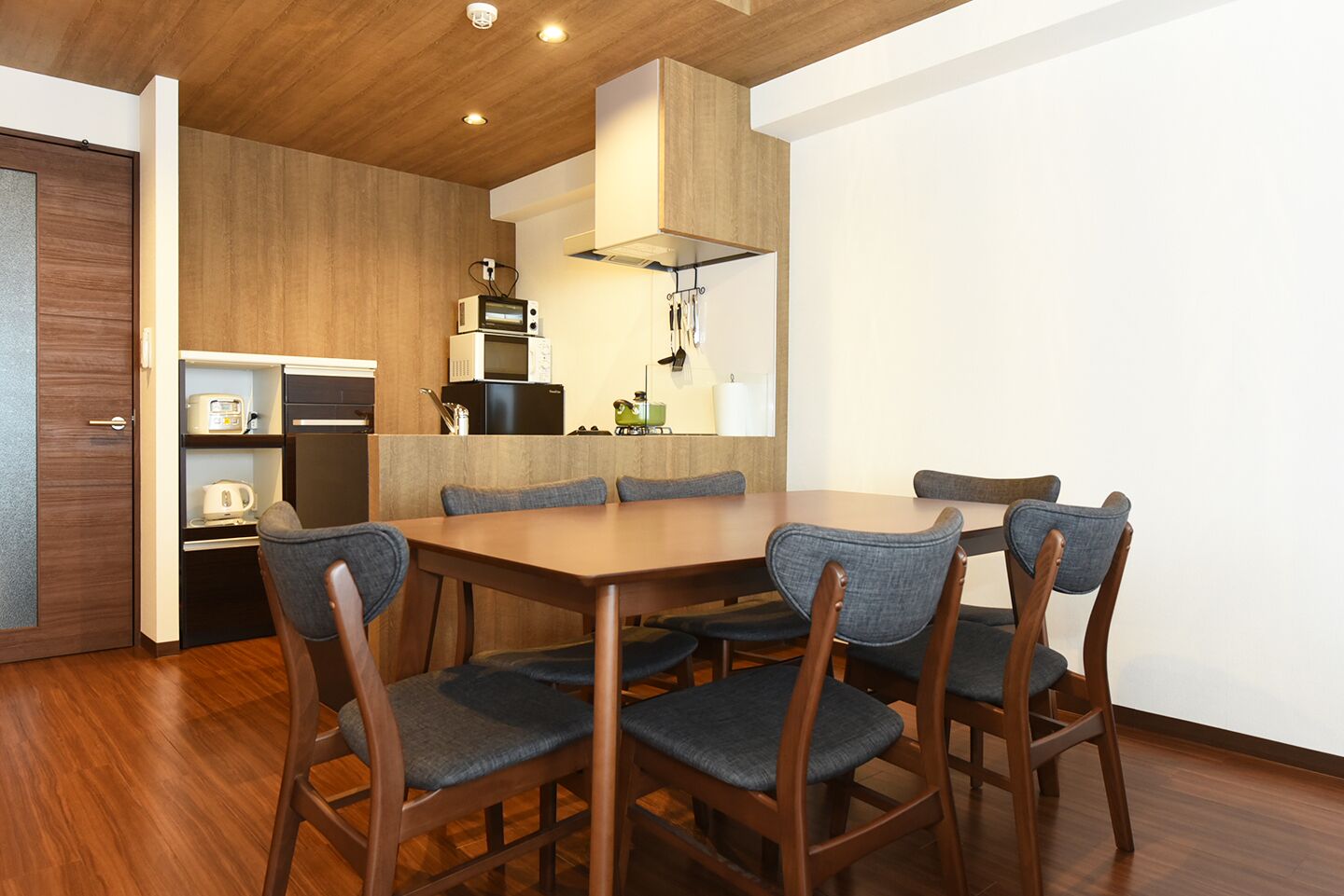 A modern kitchen with a wooden table and chairs, a microwave, and a refrigerator.