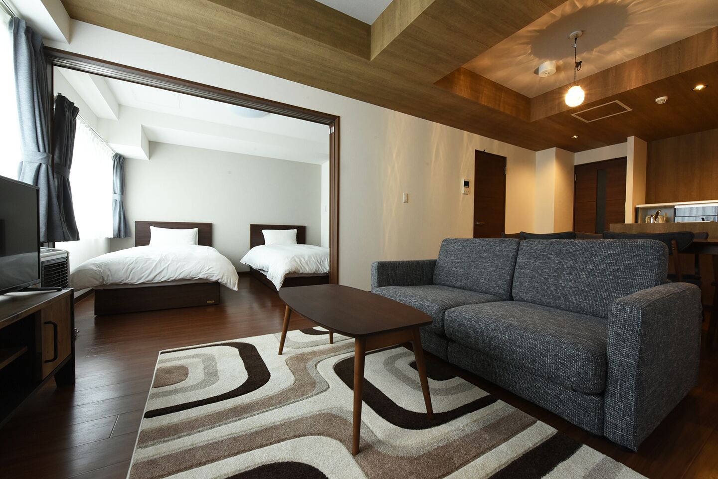 Une chambre d’hôtel moderne avec un canapé, deux lits, une télévision et un plafond en bois.
