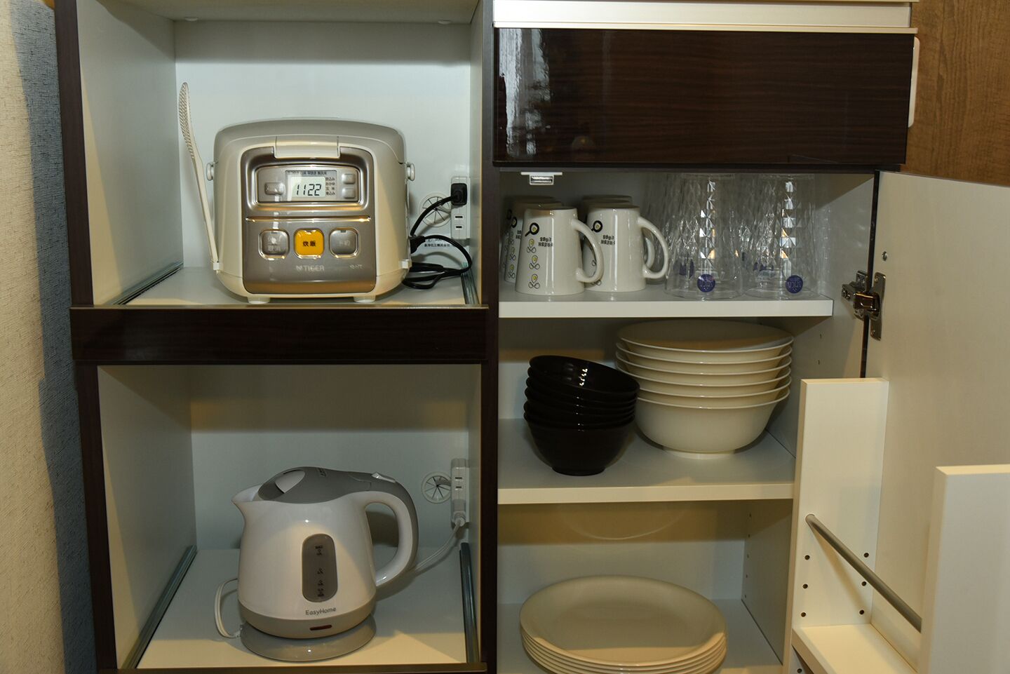 Una cocina con cafetera, hervidor y diferentes vajillas en estantes.