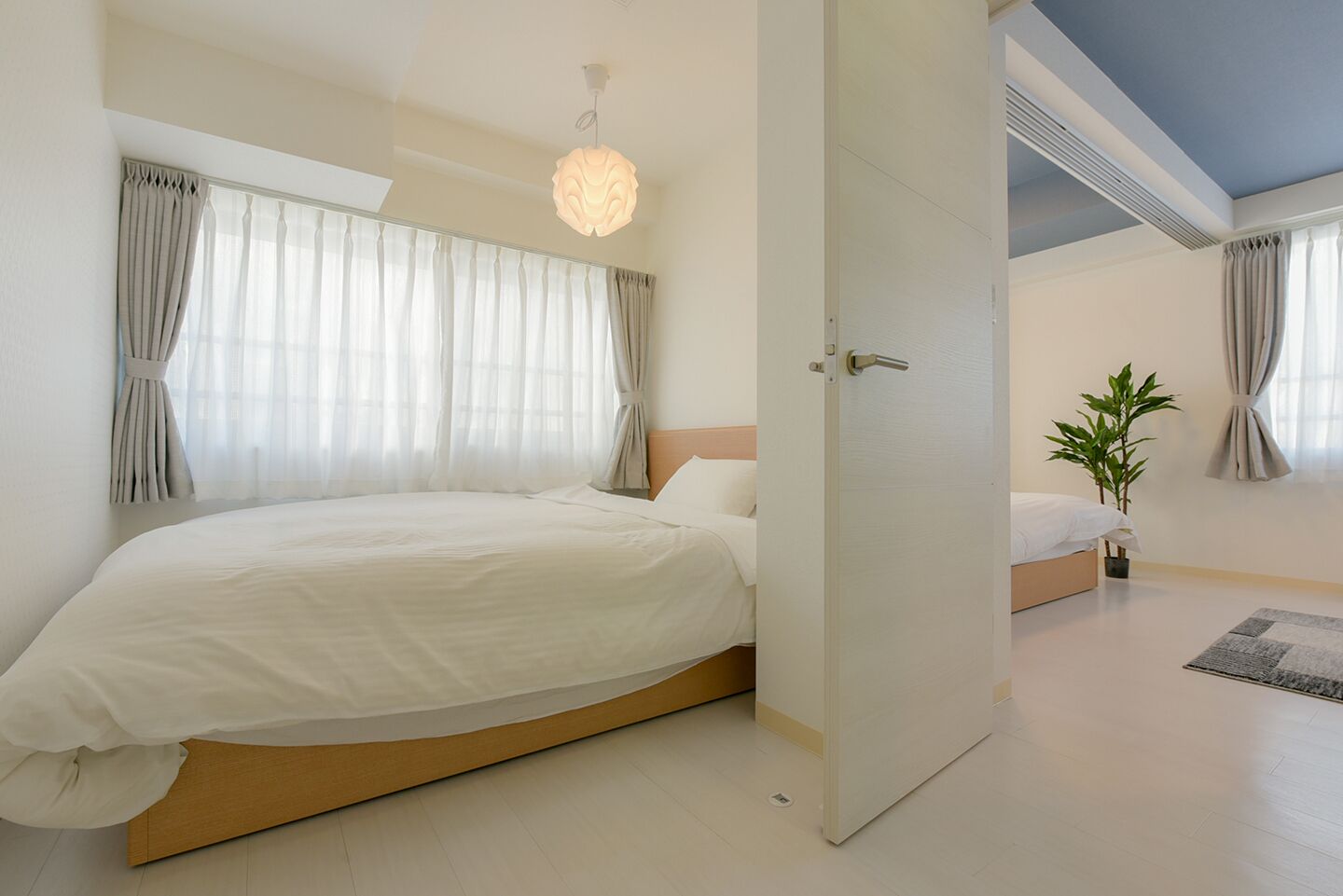 Une chambre à coucher moderne avec un grand lit, une table de chevet, un luminaire suspendu et une plante en pot.