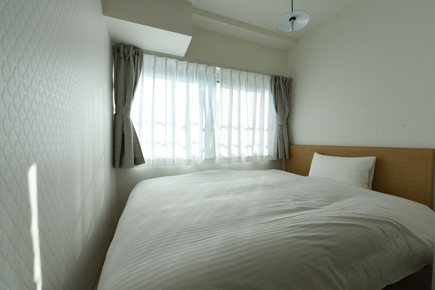 A hotel room with a large bed, a wooden headboard, and a window with sheer curtains.