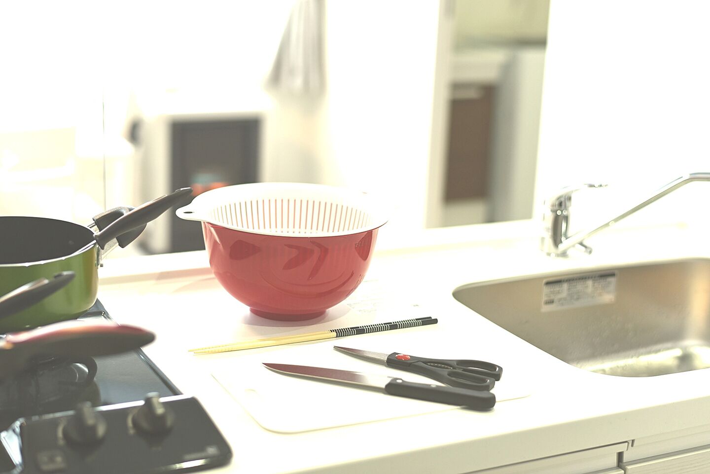 Un plan de travail de cuisine avec une passoire rouge, une casserole verte, un couteau et une paire de ciseaux.