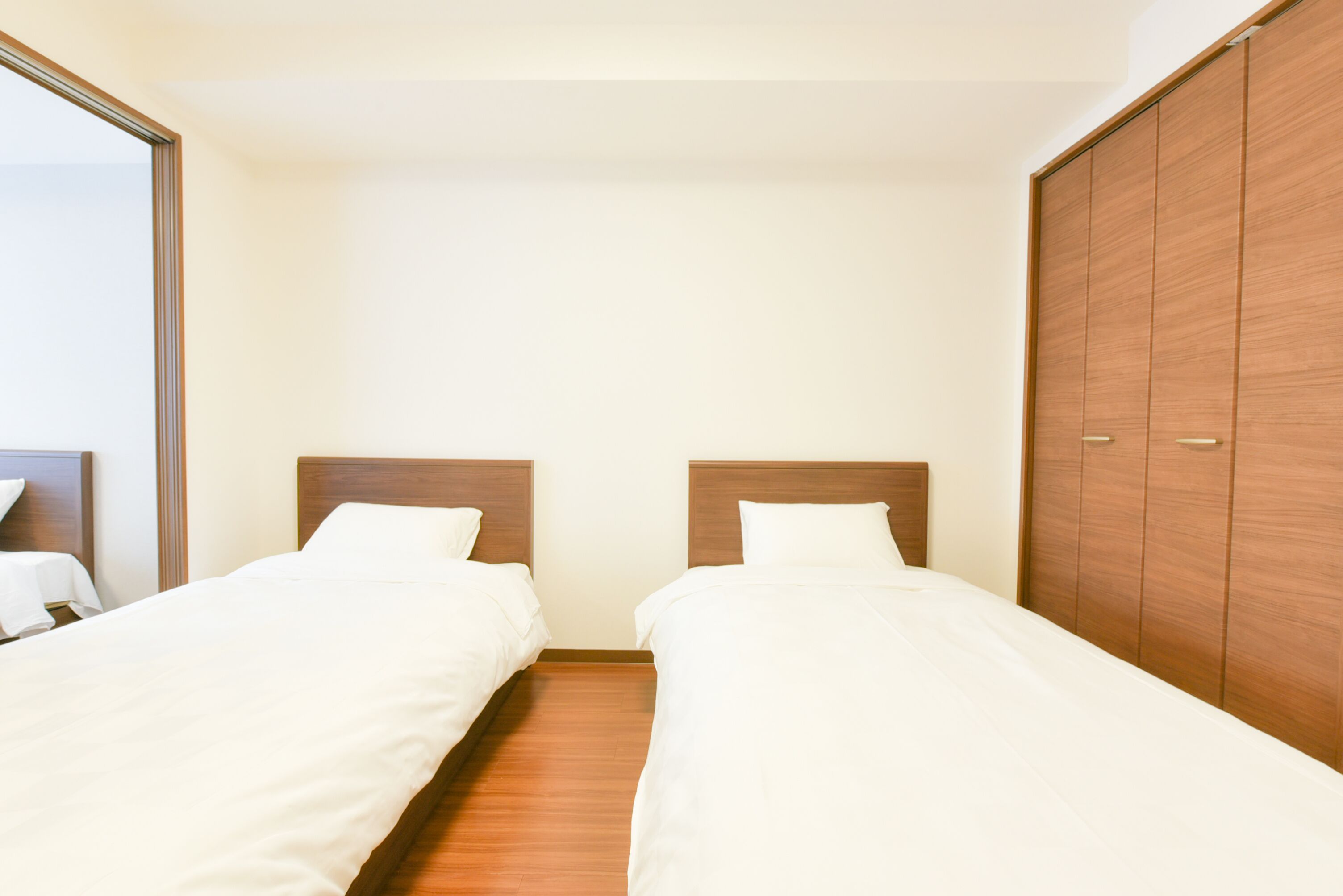 A hotel room with two single beds, wooden headboards, a wardrobe, and a large mirror.