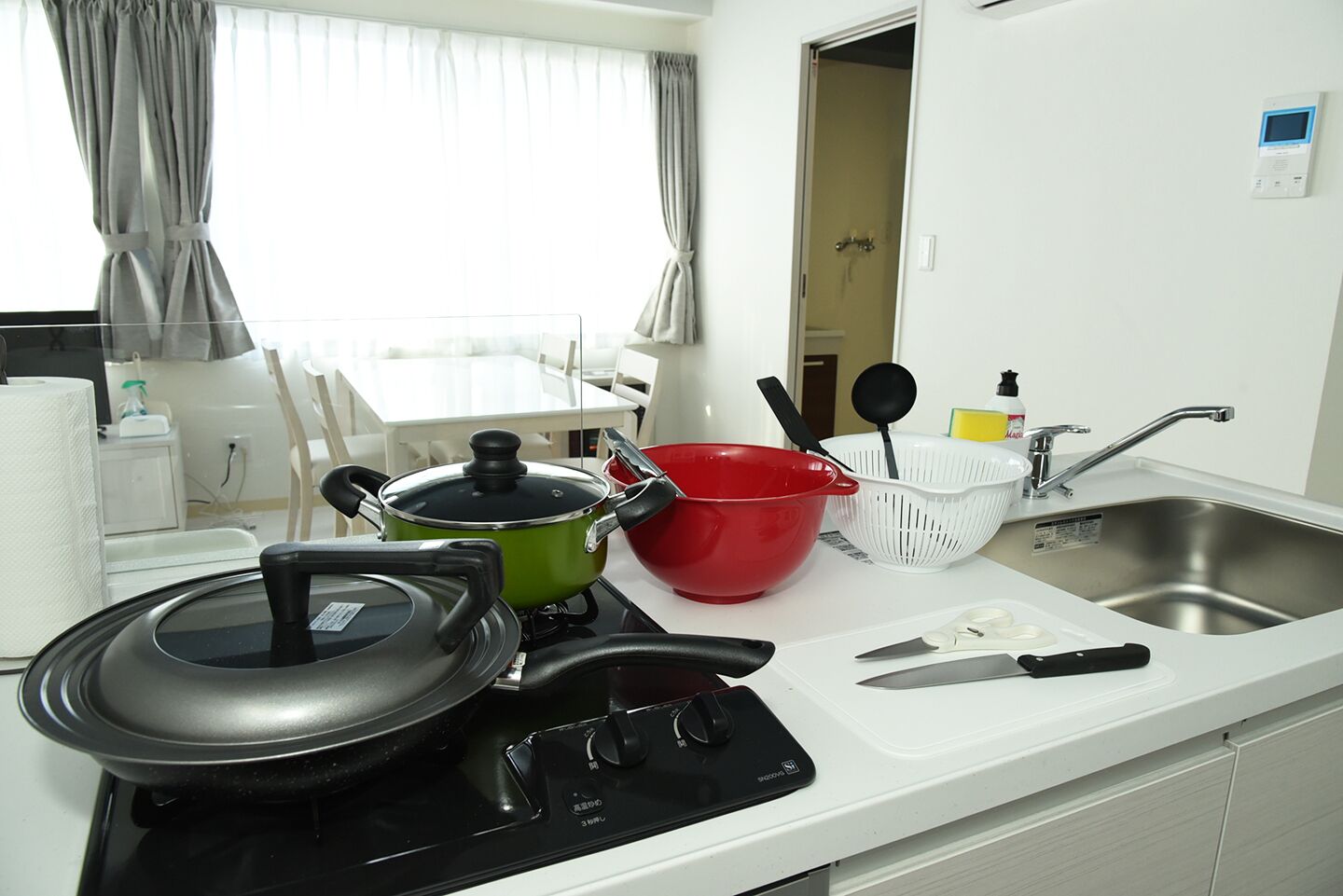 A modern kitchen with a stove, pots, a red bowl, a colander, and a sink.