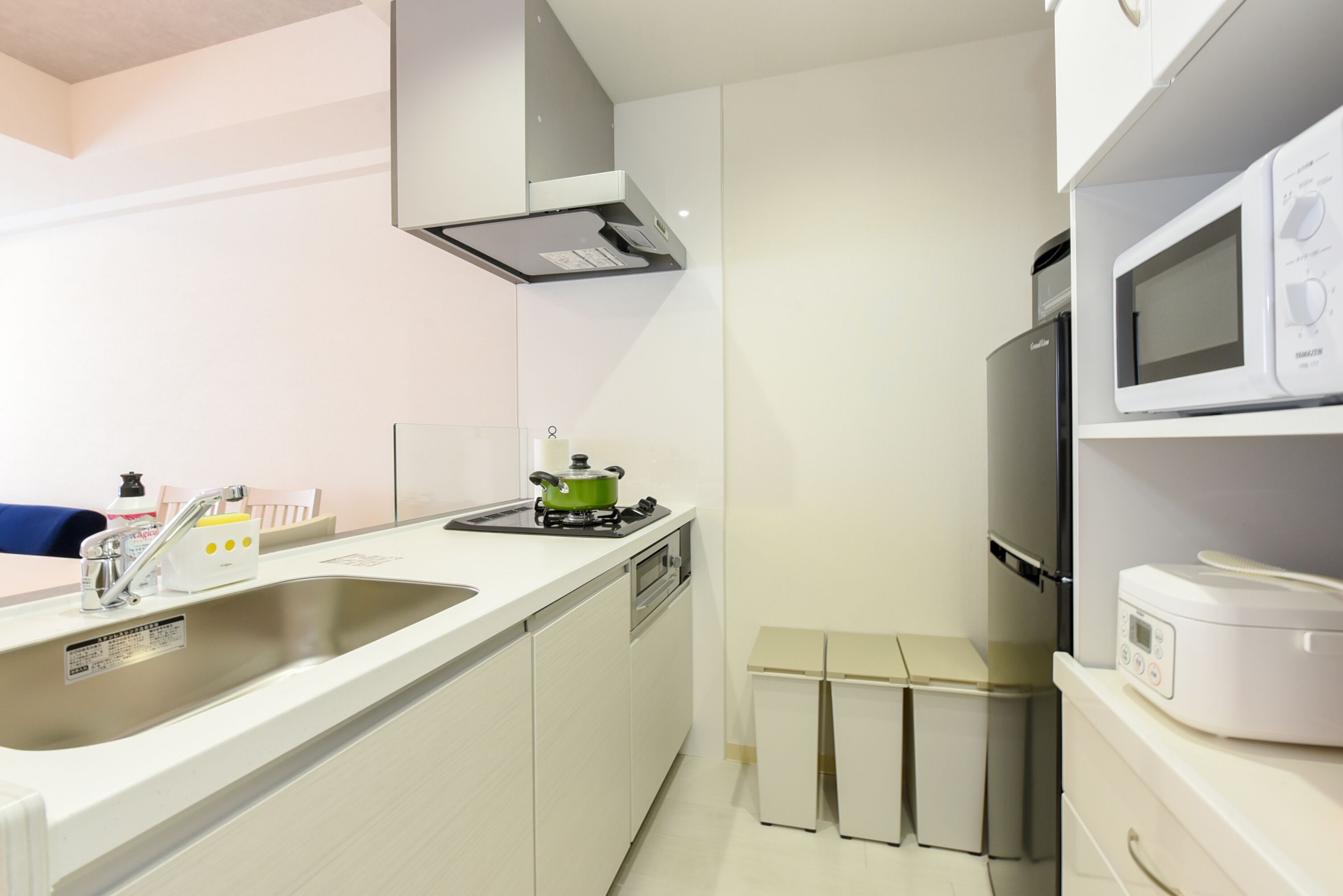 Een kleine keuken met een wastafel, fornuis, magnetron en een kleine koelkast.