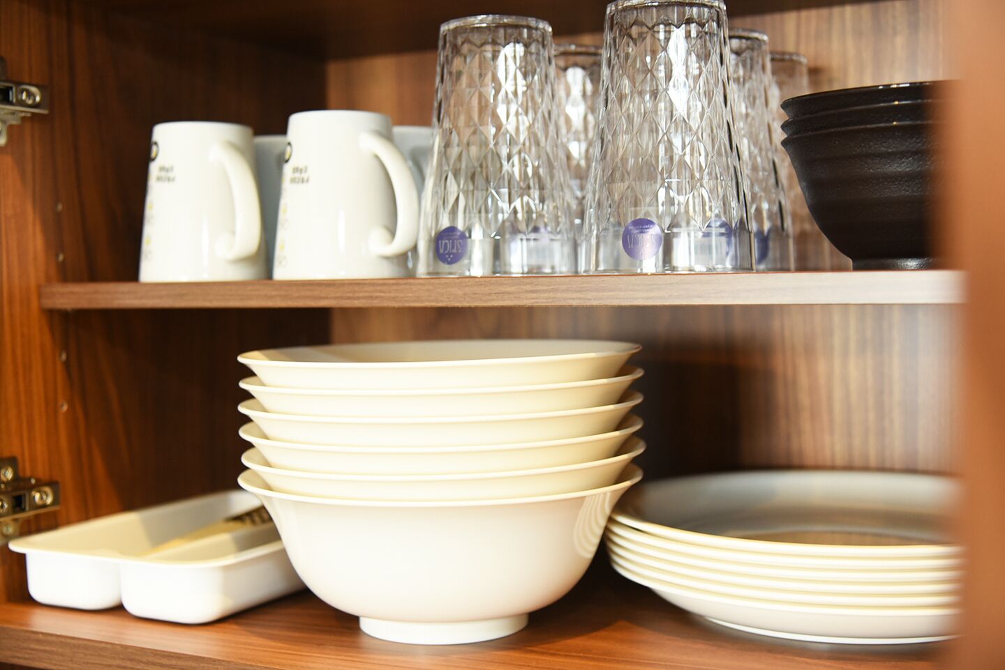 A kitchen shelf with stacked white bowls, a white coffee maker, and clear glass tumblers.